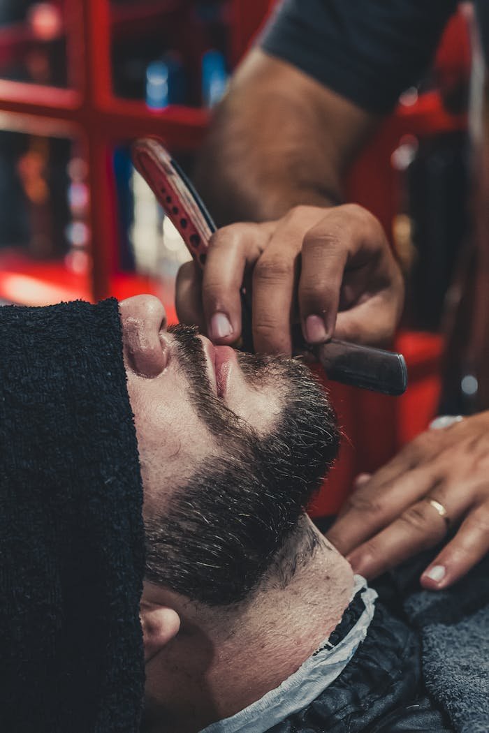 Barbería Astrabudua Erandio. A barber skillfully shaves a mans beard using a straight razor at a barbershop.